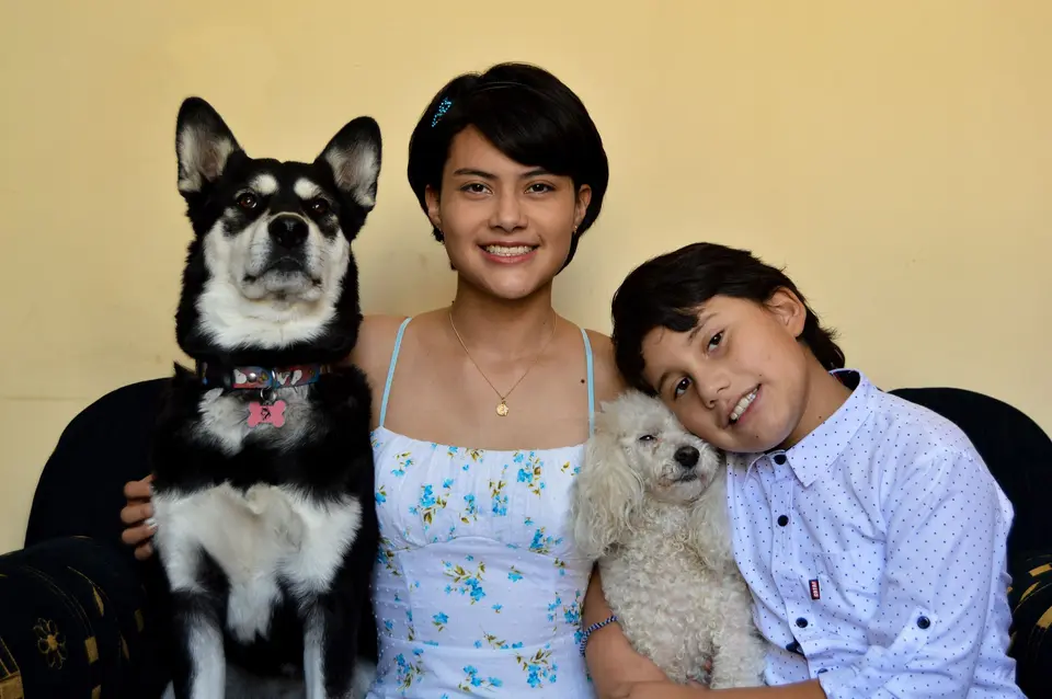 A mother and her son on a sofa with their two dogs, against a yellow wall.